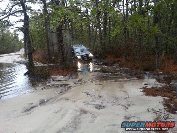 Dark 1987 Toyota 4Runner navigating a muddy forest trail with water obstacles