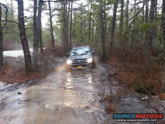 Dark gray Toyota 4Runner driving through a muddy, water-filled forest road
