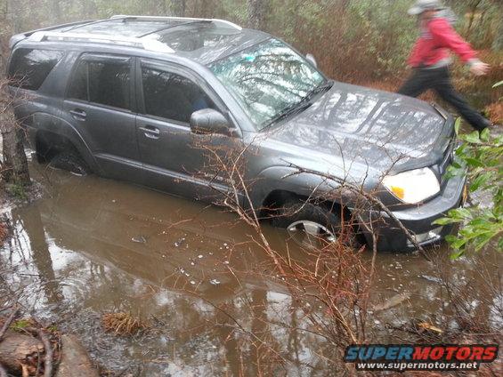 Gray SUV stuck in muddy water, person walking in background