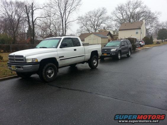 White pickup truck parked on a wet street, with a dark SUV behind it
