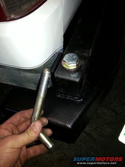 White vehicle rear bumper with black trailer hitch and a hand holding a metal pin