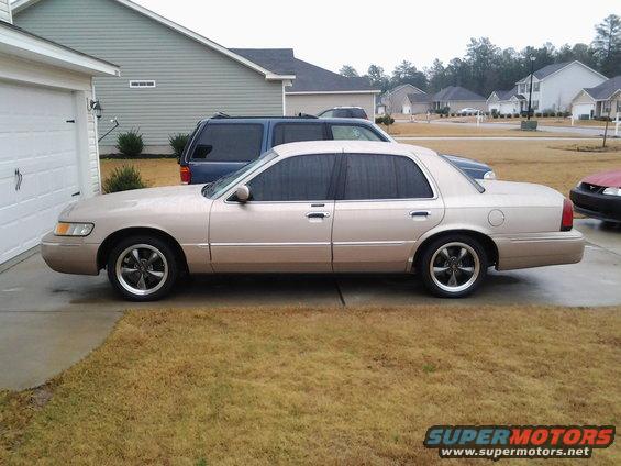 1998 Mercury Grand Marquis sedan parked in driveway next to a garage and a blue SUV