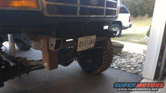 Custom bumper mount attached to the frame of a truck, with a license plate visible. Another white SUV is parked in the background