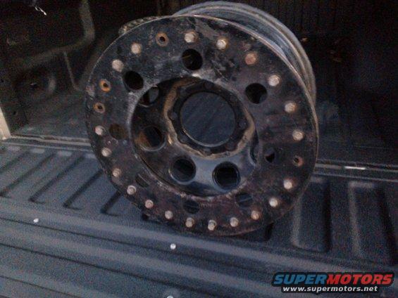Black wheel with numerous lug nut holes, resting in a truck bed