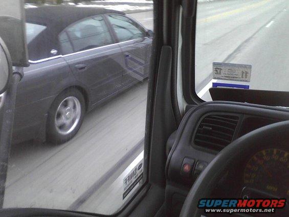 Side view of a dark sedan driving on a road, seen from inside another vehicle
