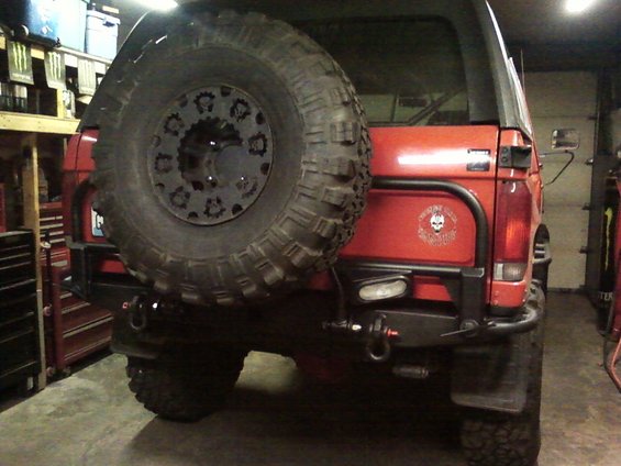 Rear view of a red SUV with a large spare tire mounted on the back. It has a custom bumper and a skull decal on the tailgate