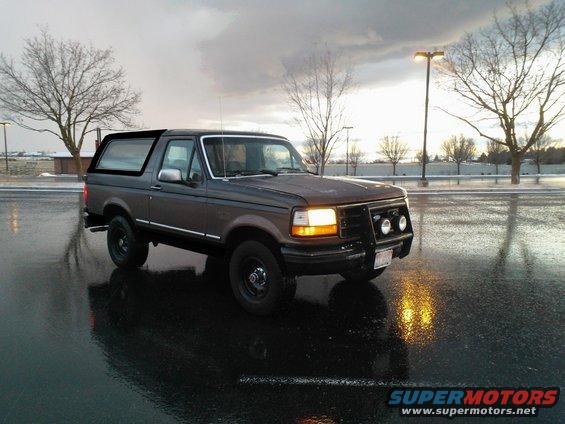 Dark brown Ford Bronco parked on wet asphalt, cloudy sky