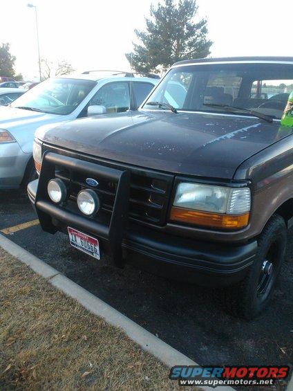 Dark brown 1992 Ford Bronco with a black bull bar and auxiliary lights, parked next to a silver SUV