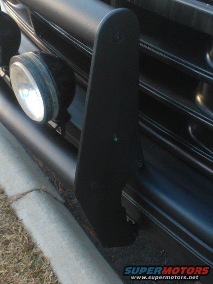 Close-up of a black brush guard attached to a vehicle's front grille, with two round lights visible