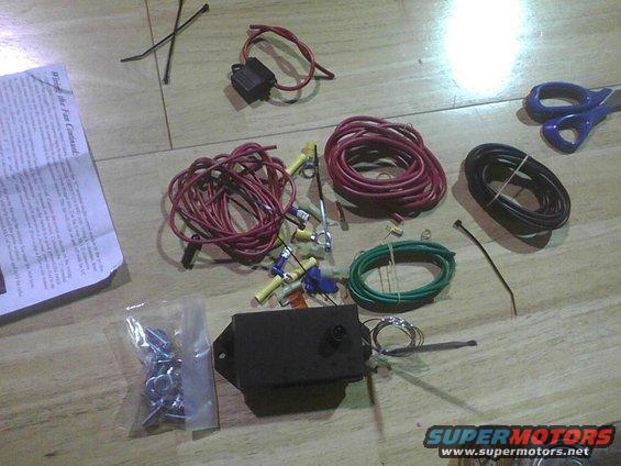 Wiring kit with red, green, and black wires, fuse holder, connectors, screws, and scissors on a wooden surface