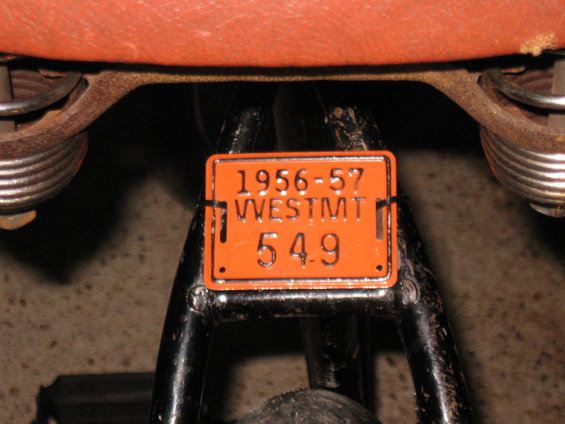 Orange license plate from 1956-57 Westmt 549 attached to a motorcycle seat spring