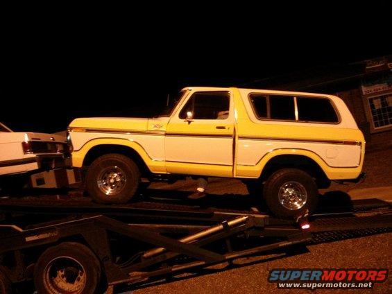 Yellow and white Ford Bronco on a trailer, next to another vehicle