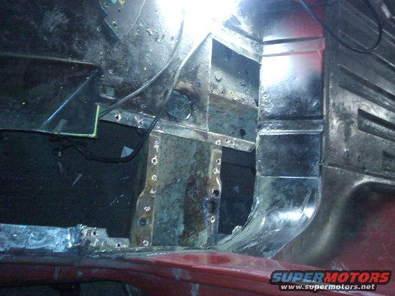 Rusted metal interior of a red vehicle, showing structural damage and repair work
