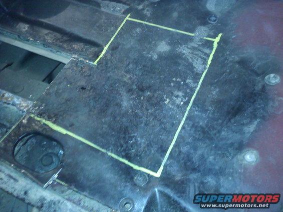 Metal floor panel with yellow chalk lines indicating a cut area. Some rust and bolts are visible