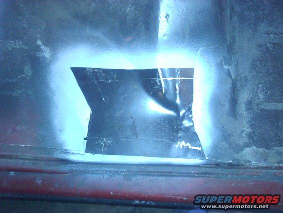 Metal patch covers hole in red car body panel, spray paint around edges