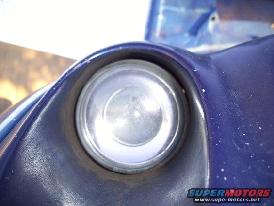Close-up of a blue car's round headlight assembly with a dark bezel