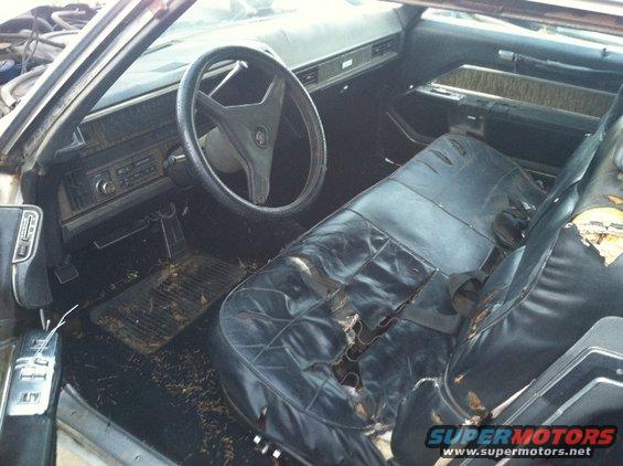 Interior of a 1970s Cadillac with torn black leather seats and a cracked steering wheel