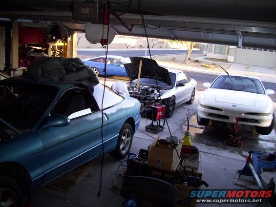 Three Ford Probes in a garage, two with hoods open. One blue, one silver, one white