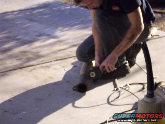 Man using an angle grinder on a rusty exhaust pipe section