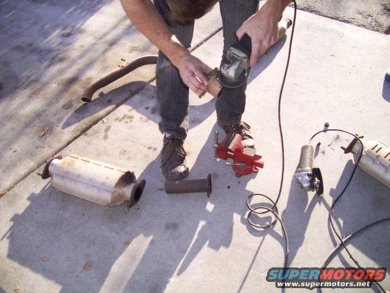 guy cutting exhaust pipe with angle grinder, catalytic converter on ground