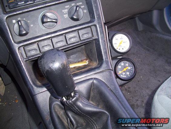 Car interior center console with gear shifter, climate controls, and two aftermarket gauges mounted to the right