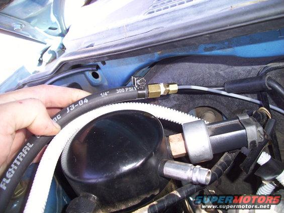 Close-up of engine bay with hand holding hose marked 1/4" 300 PSI