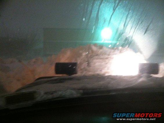 Dashboard view through a snow-covered windshield with bright lights ahead