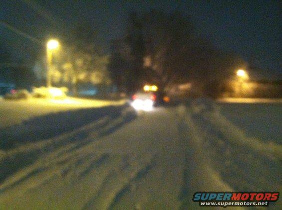 Car with illuminated taillights driving on a snow-covered road at night