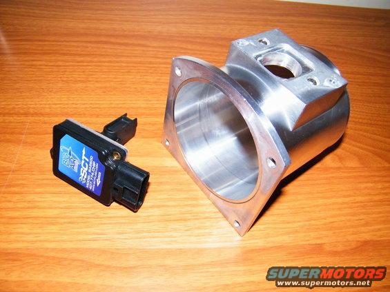 SCT MAF sensor next to a polished aluminum intake manifold adapter on a wooden surface