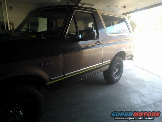 Side view of a brown and white Ford Bronco parked in a garage. It has a yellow and green stripe along the lower body