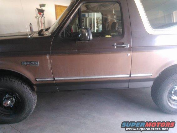 Side view of a brown 1992 Ford Bronco parked indoors. The word "BRONCO" is visible on the fender
