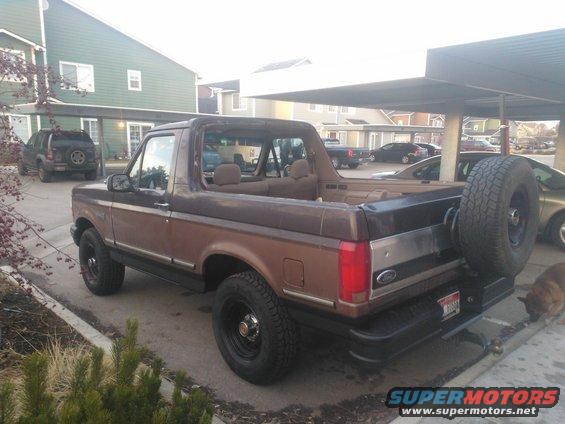 Brown Ford Bronco parked outside, with a spare tire on the back. Another SUV is parked in front