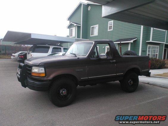 Dark brown 1992 Ford Bronco parked under a carport, spare tire visible in the bed