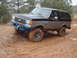 1990 Ford Bronco - A two-tone Ford Bronco navigates a muddy off-road course during light snowfall.
