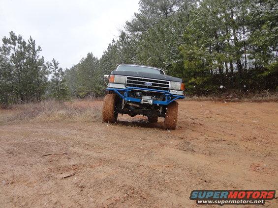 Ford F-Series truck with blue aftermarket bumper and winch, on a muddy dirt road