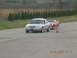 2003 Ford Crown Victoria - A silver 2003 Ford Crown Victoria sedan is followed by a red convertible on a paved track.