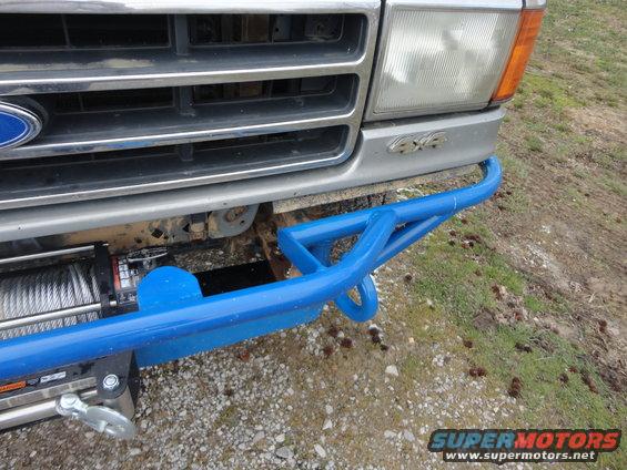 Ford Bronco front end with custom blue bumper and winch. Grille is silver, headlights are clear. "4x4" badge visible