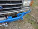 1990 Ford Bronco - Front view of a Ford Bronco with a custom blue bumper and winch, showing the grille and headlights.