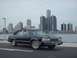 1991 Mercury Grand Marquis - A black sedan is parked by the water with the Detroit skyline visible behind it.