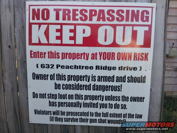 No Trespassing Keep Out sign with address and warning about armed owner