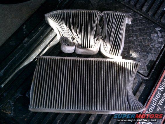 Three dirty cabin air filters, one large and two smaller ones, sitting on a black mat