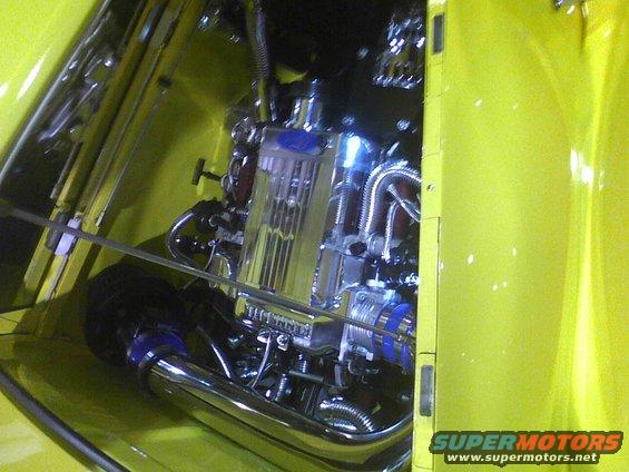 Yellow vehicle engine bay with chrome and blue accents, custom modifications visible