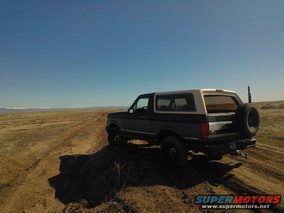 1992 Ford Bronco driving on a dirt trail with mountains in the distance