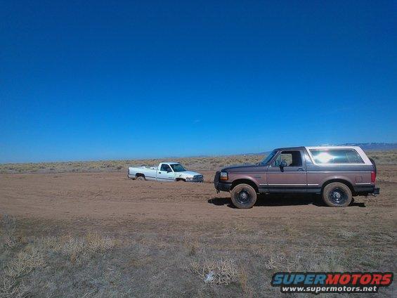 1992 Ford Bronco parked on dirt, white truck stuck in background
