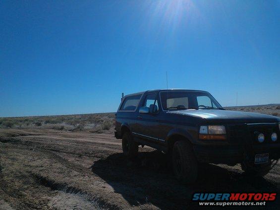 Dark blue Ford Bronco parked on a dirt road under a bright sun