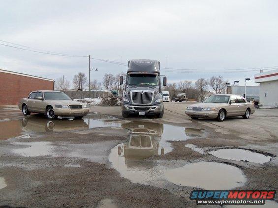 2000 Mercury Grand Marquis sedans parked near a semi-truck in a wet lot