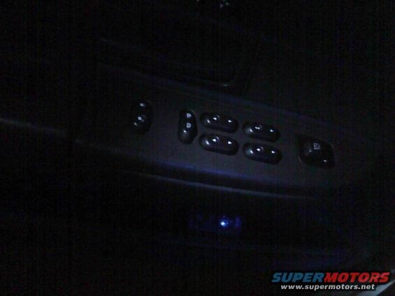 Car interior door panel with illuminated window controls and a small blue light