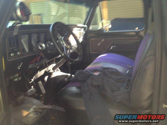 Interior shot of a vintage truck, showing the dashboard, steering wheel, and seats with purple and gray covers