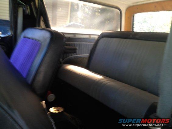 Interior shot of a vehicle showing front seats with purple inserts and a gray bench seat in the back. Sunlight streams through the windows