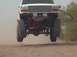 1992 Ford Bronco - This lifted truck is airborne, its suspension and tires against a dusty background.